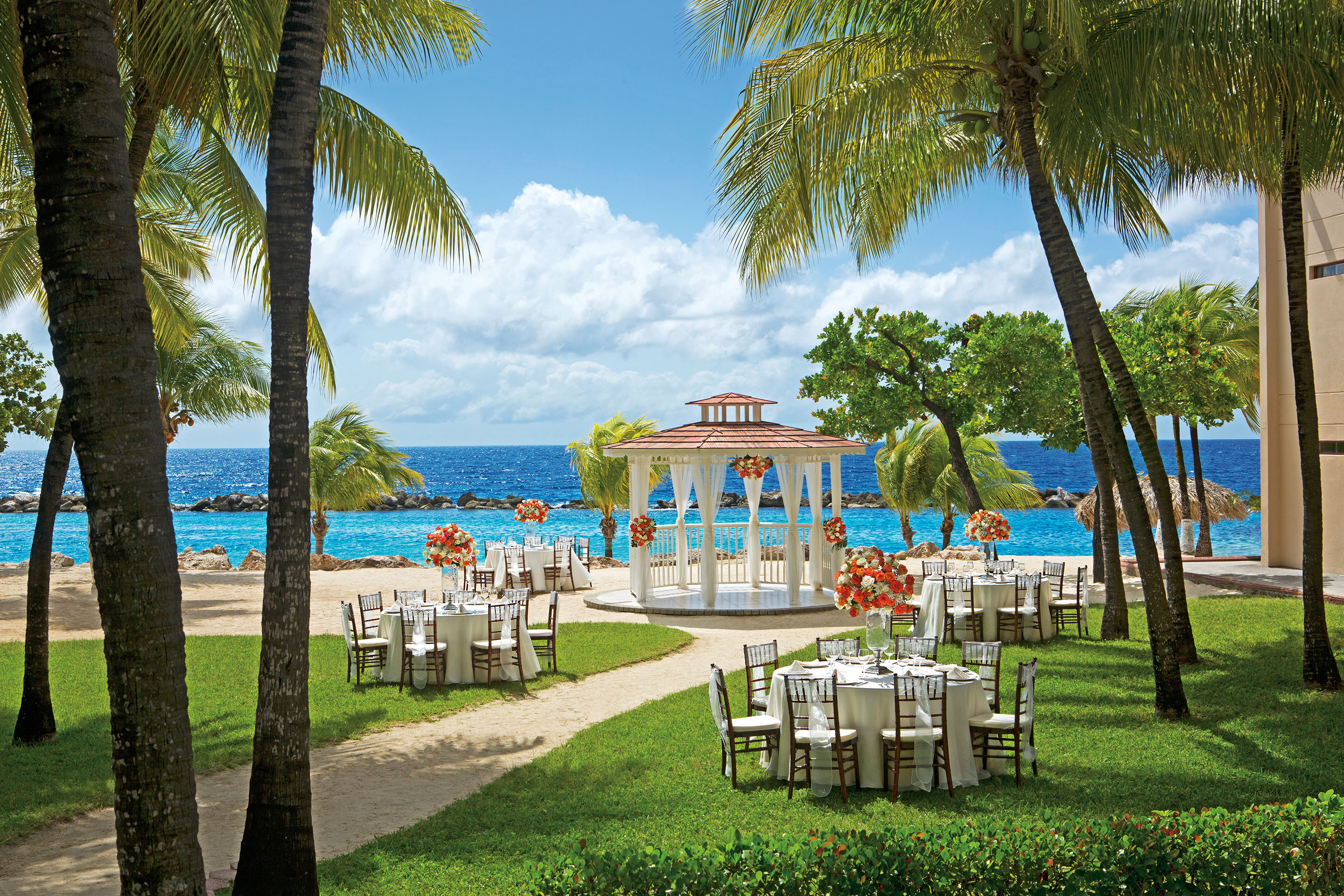 Romantic wedding gazebo and tables set in secluded area.  Surrounded by palm trees and set along a bright blue oceanscape.