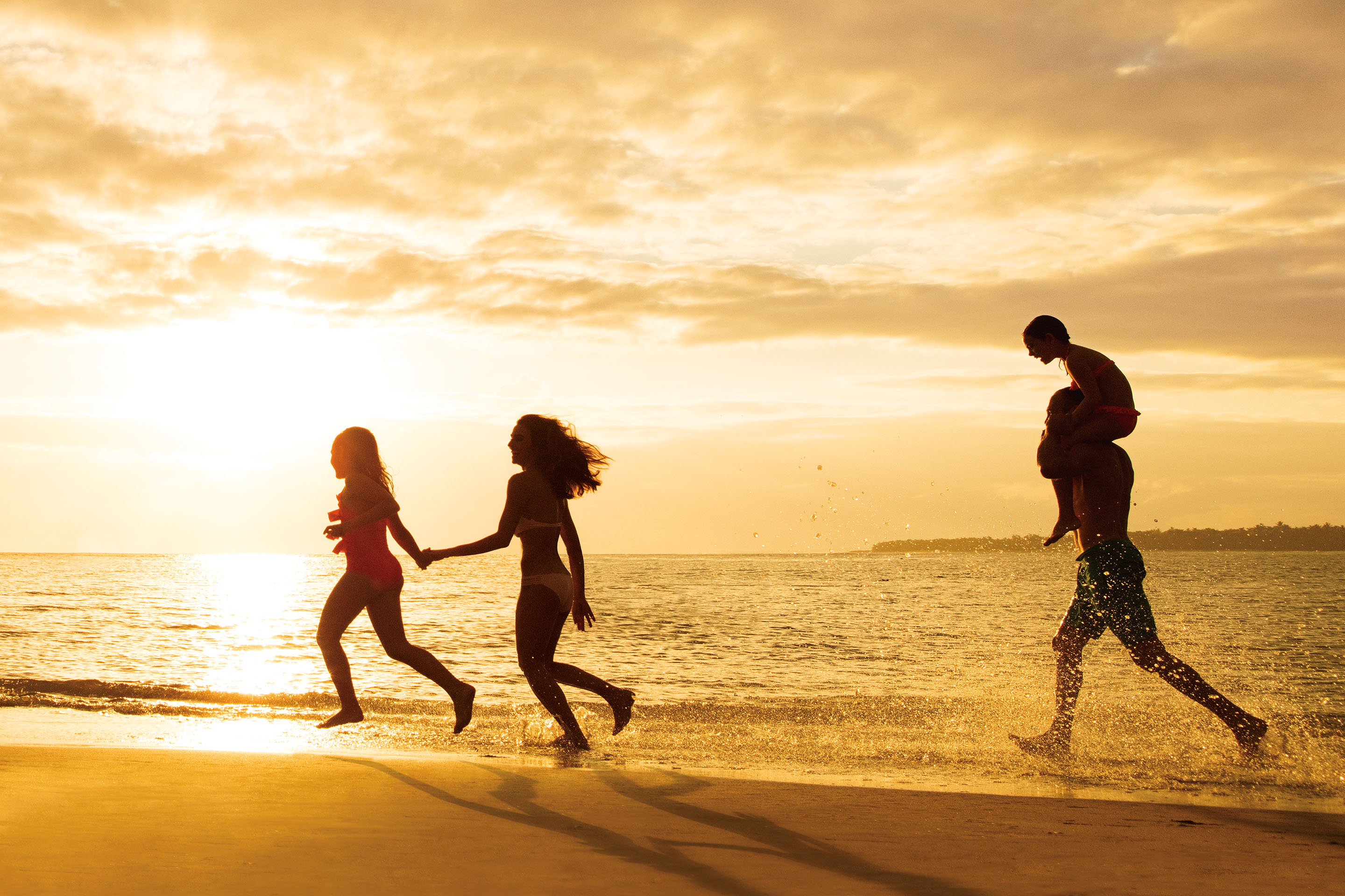 Father and three daughters running on the beach at sunset